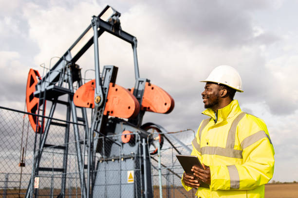 Oil field worker monitors drilling operations on oil rig with tablet and helmet.Portrait of an oil field worker standing in front of oil rigs drilling crude oil.