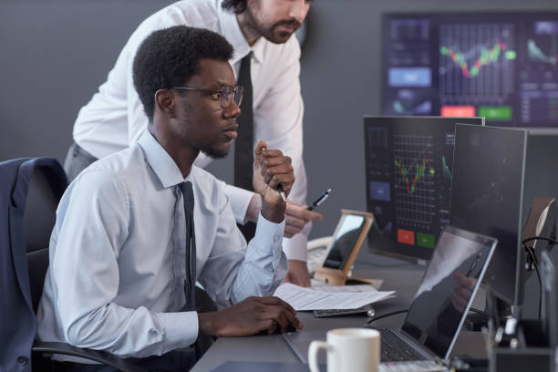 Young brokers waiting for high indicators looking at computer monitors while sitting at table in broking office